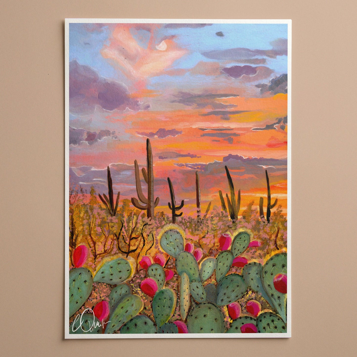 Framed artwork of a desert landscape with cacti and a sunset sky on a beige wall.
